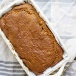 overhead photo of a loaf of sourdough pumpkin bread in a parchment lined stone bread pan on top of a blue and white stripped towel on a wood table