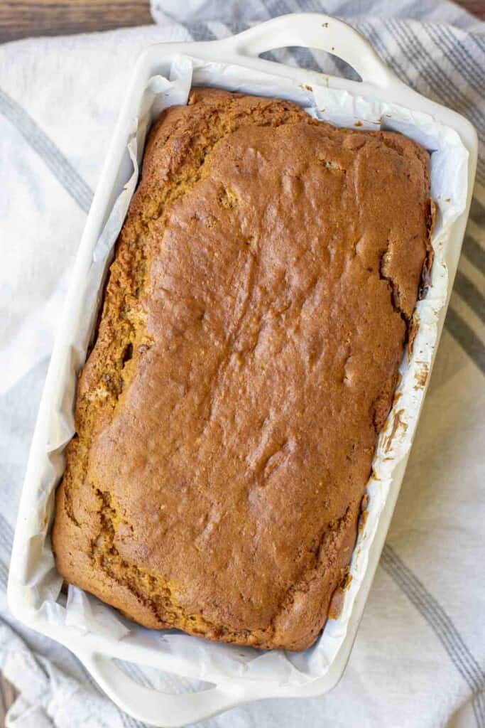 overhead photo of sourdough pumpkin bread in a cream stone loaf pan on a white and blue stripped towel