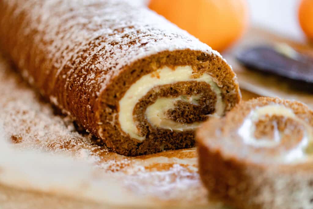 sourdough pumpkin roll with cream cheese filling swirled on the inside on a [piece of parchment paper with cut slices to the right