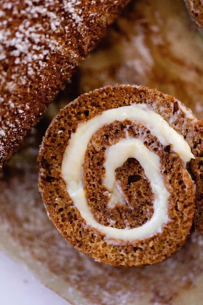 close up of pumpkin cake rolled with with cream cheese frosting filling on the inside. The roll is on parchment paper