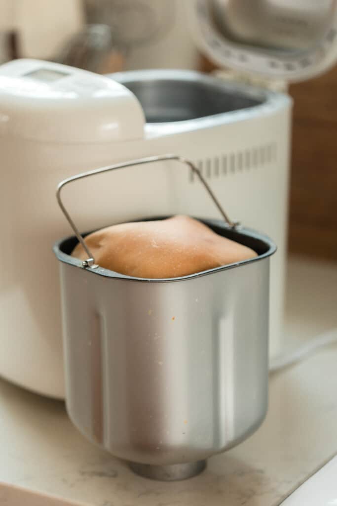 sourdough bread in a stand machine baking pan on the countertop with a bread machine in the background