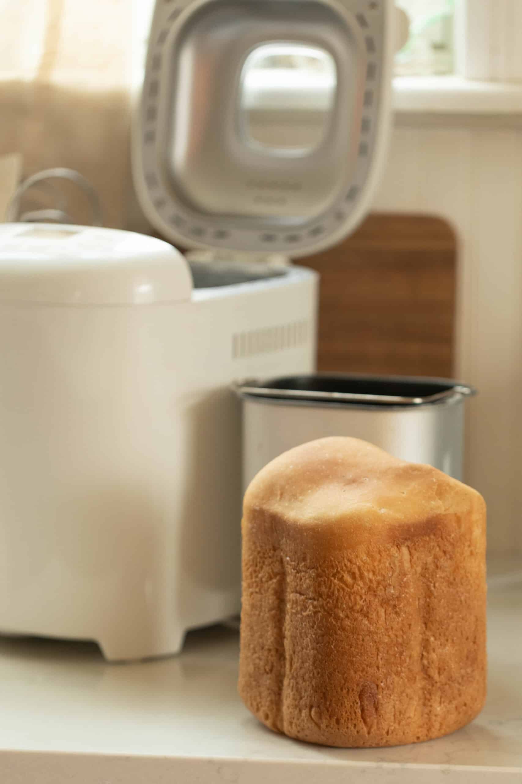 sourdough bread right out of the bread machine on a white countertop with the bread machine and baking pan in the background