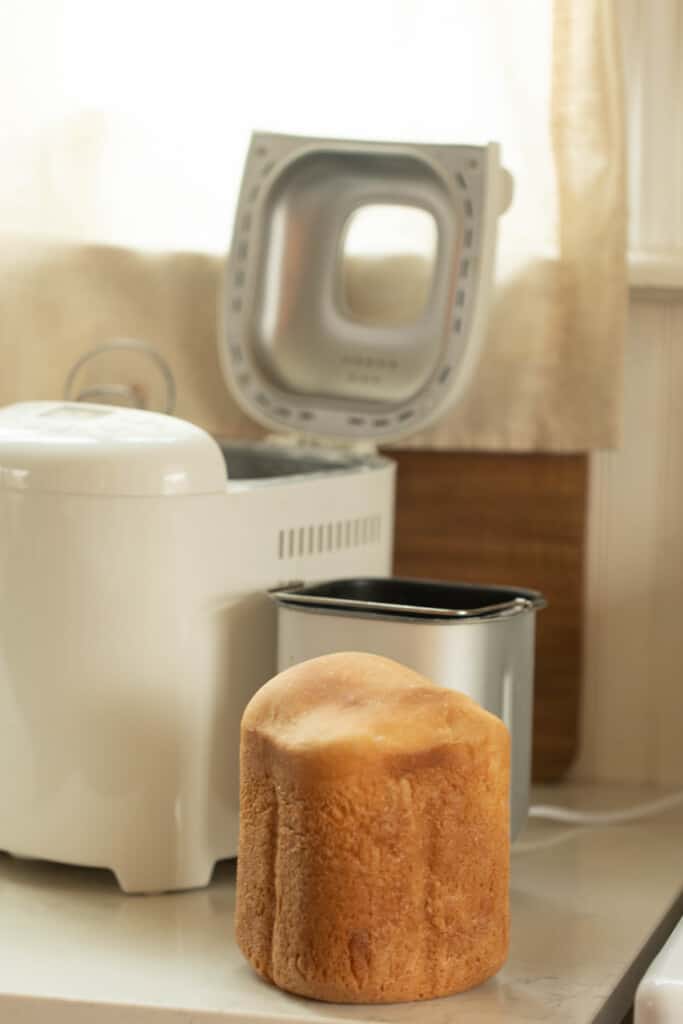 loaf of sourdough bread fresh out of the bread machine with the bread machine in the background