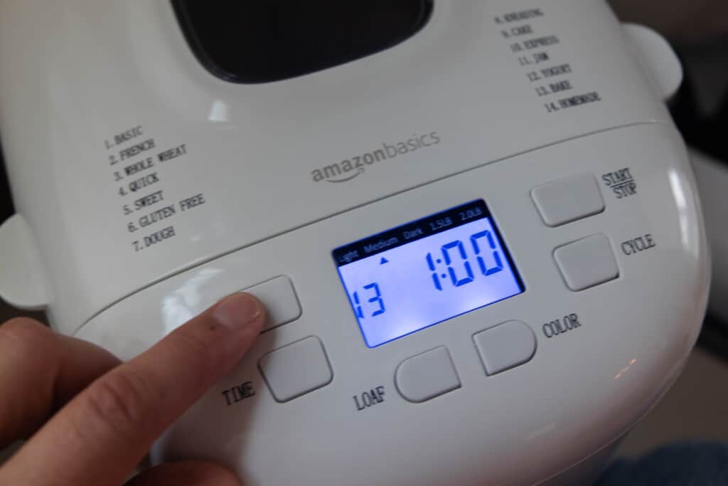 hand pressing the menu button on a white bread machine