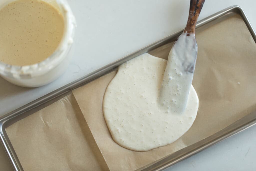 sourdough starter on parchment lined sheet with a wooden spatula in the starter