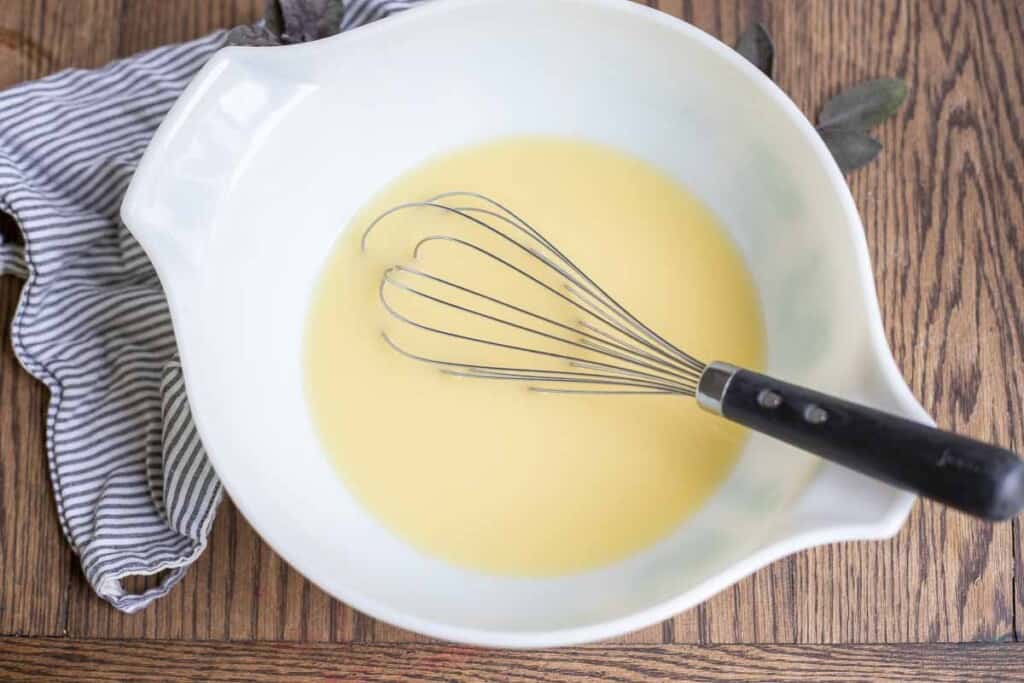 Eggs and broth whisked together in a vintage Pyrex bowl with a whisk resting gin the bowl.