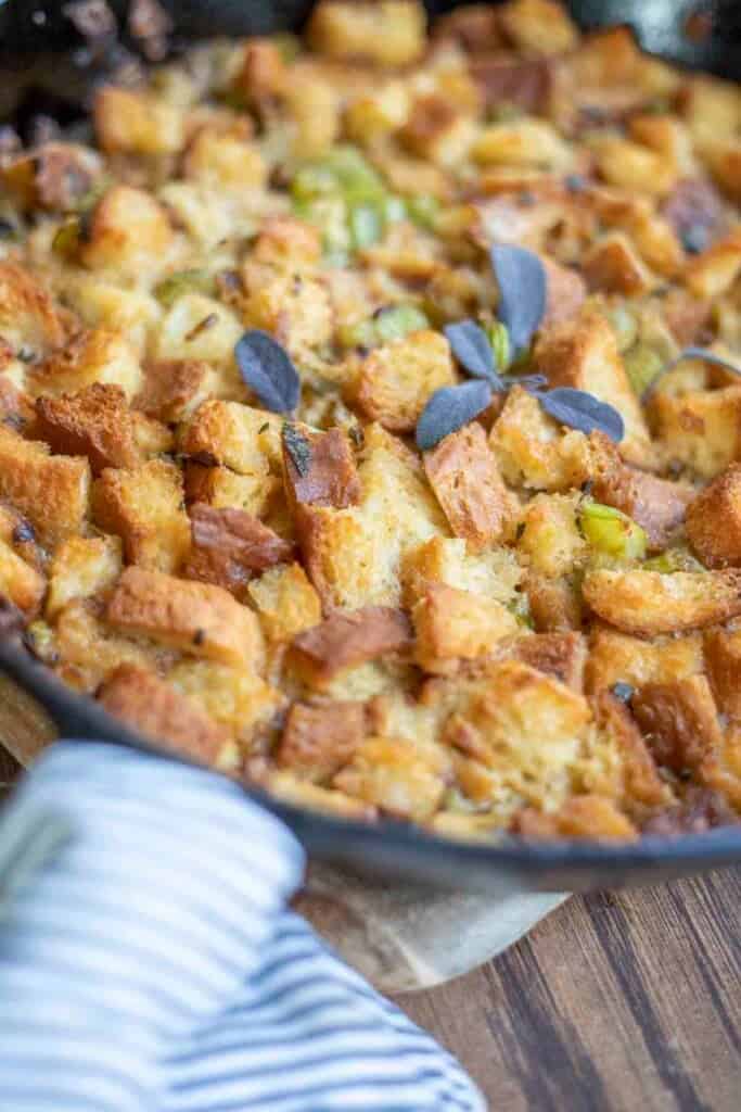 gluten free sourdough stuffing in a cast iron skillet. A blue and white stripped towel is wrapped around the handle of the skillet