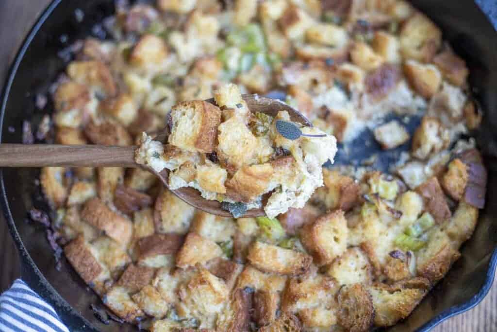 gluten free stuffing in a cast iron skillet with a spoon of stuffing being held in front of the skillet