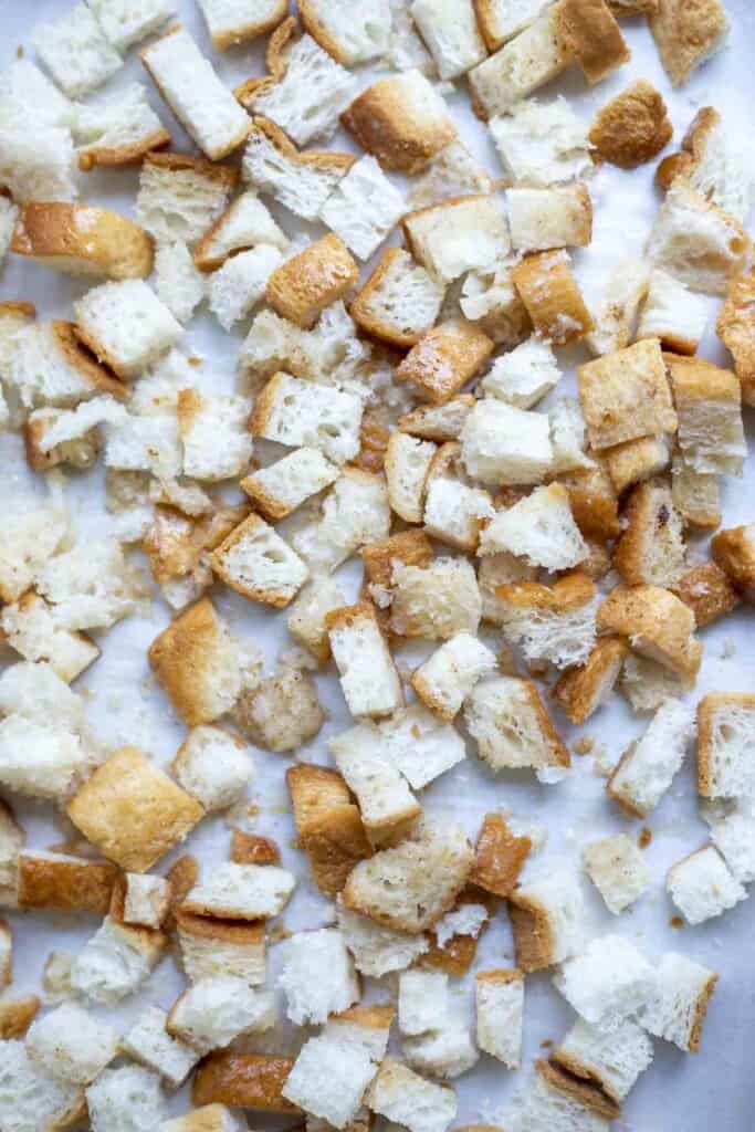 Gluten free bread cut into cubes on a parchment lined baking sheet.