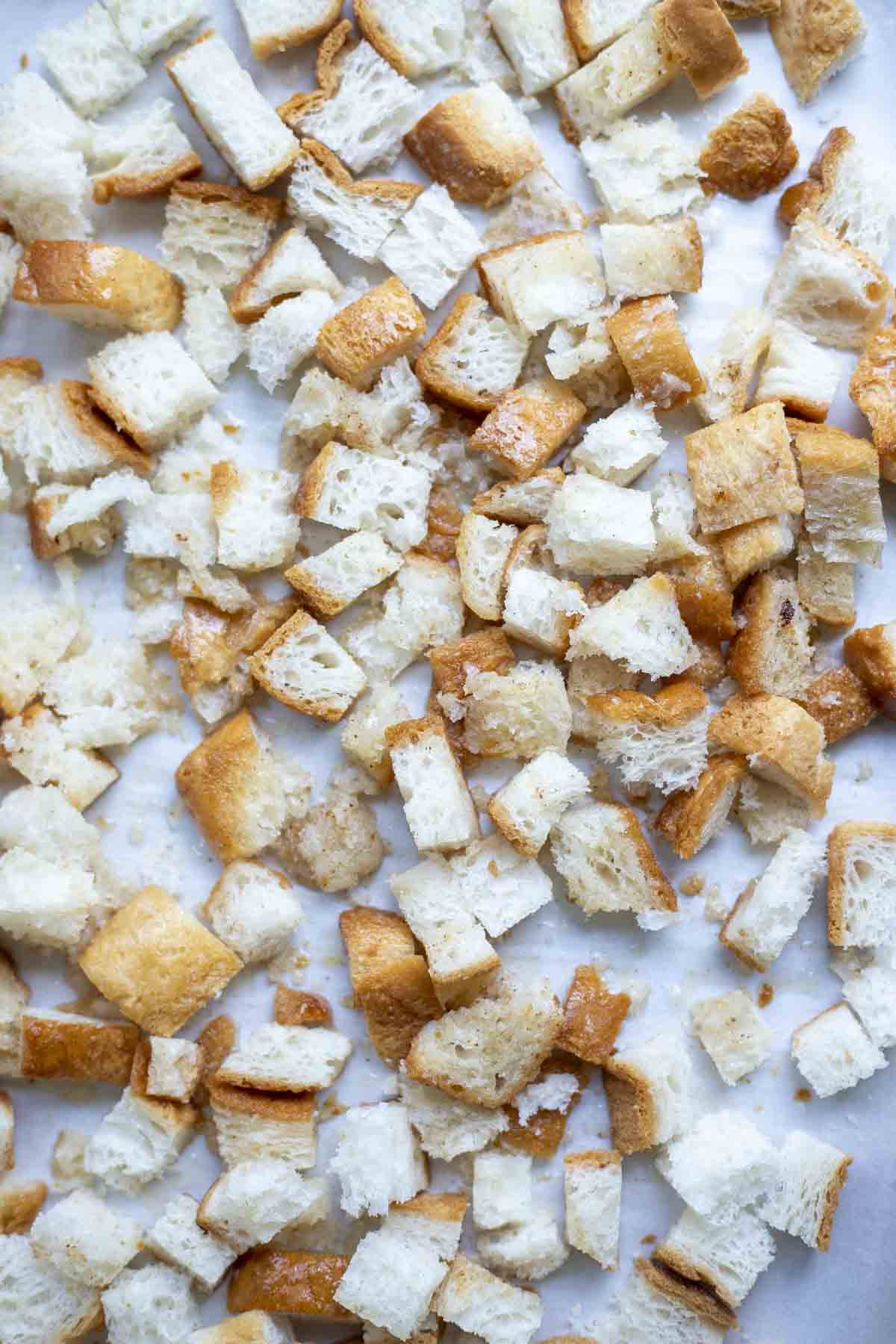 Gluten free bread cut into cubes on a parchment lined baking sheet.