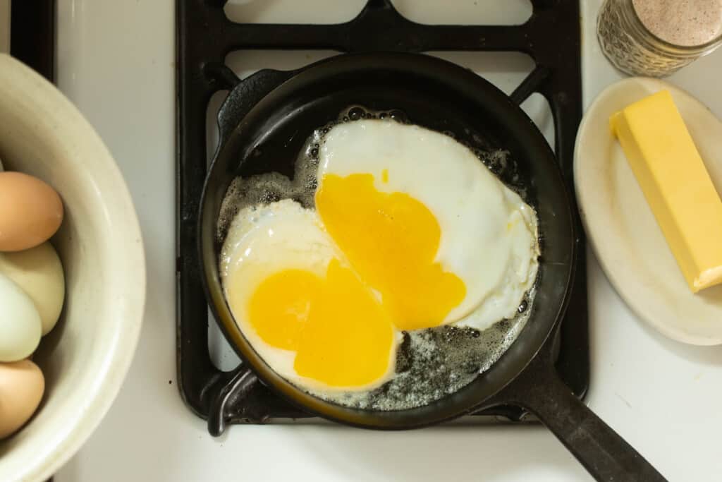 egg cracked into a small cast iron skillet with a bowl of eggs to the left