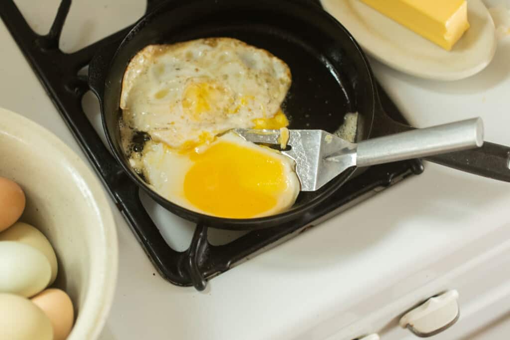 spatula under a fried egg ready to flip over in a skillet