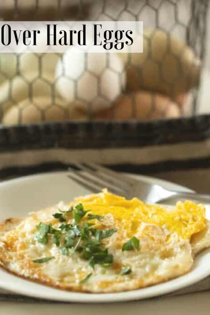 over hard fried eggs topped with chives on a white plate. A basket of farm fresh eggs are in the background