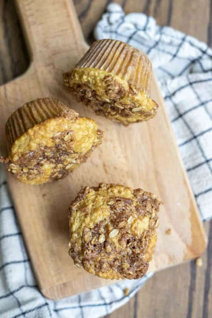 three sourdough banana muffins with a brown sugar oat crumble on top of a wood cutting board on a white and black towel