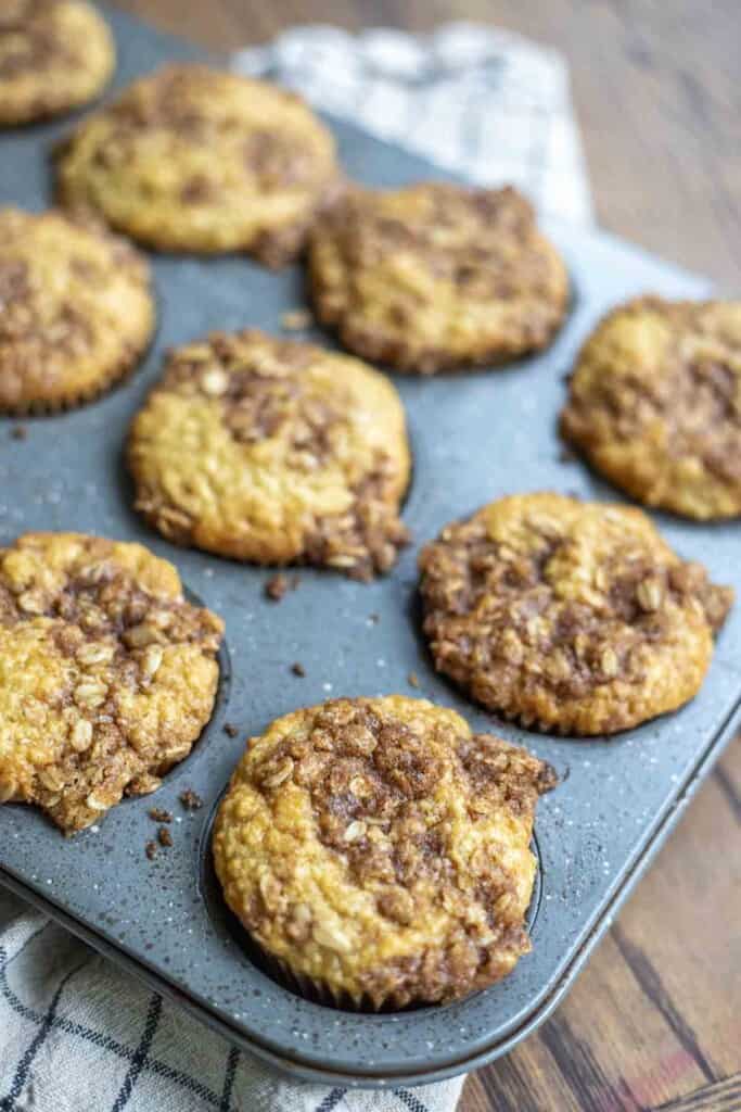 sourdough banana muffins with a brown sugar oat crumble in a gray muffin tin on a white and black checked towel