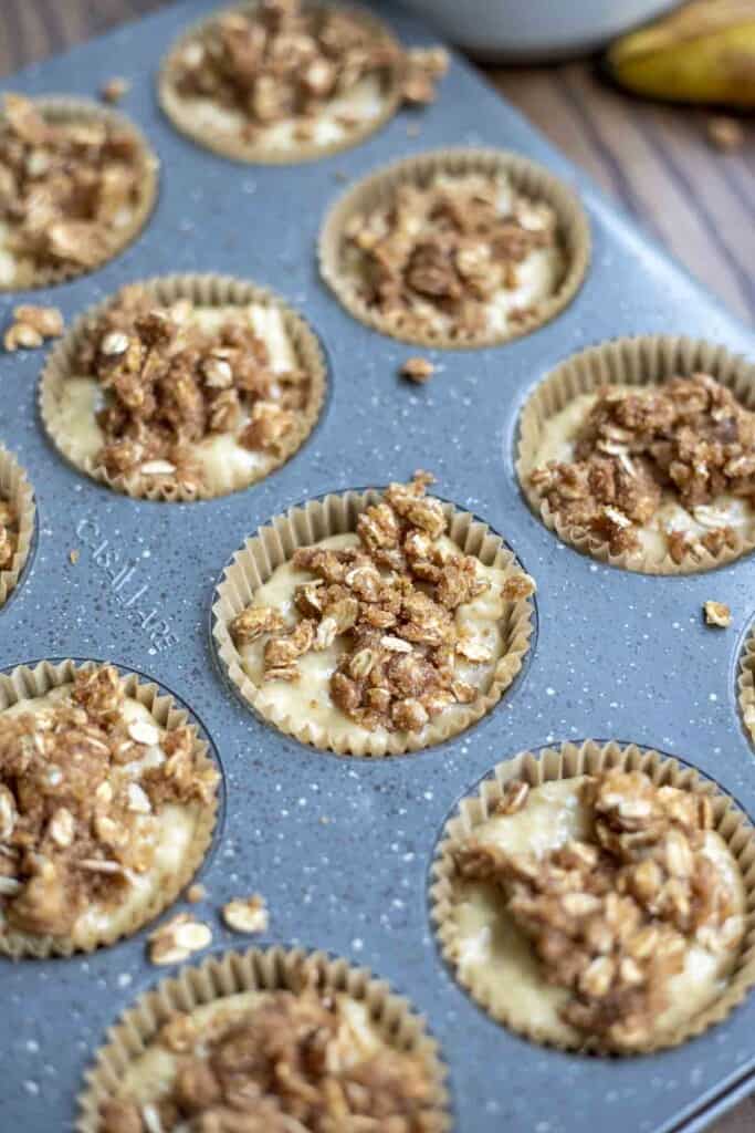 sourdough banana muffin batter topped with oat crumble in a lined muffin pan