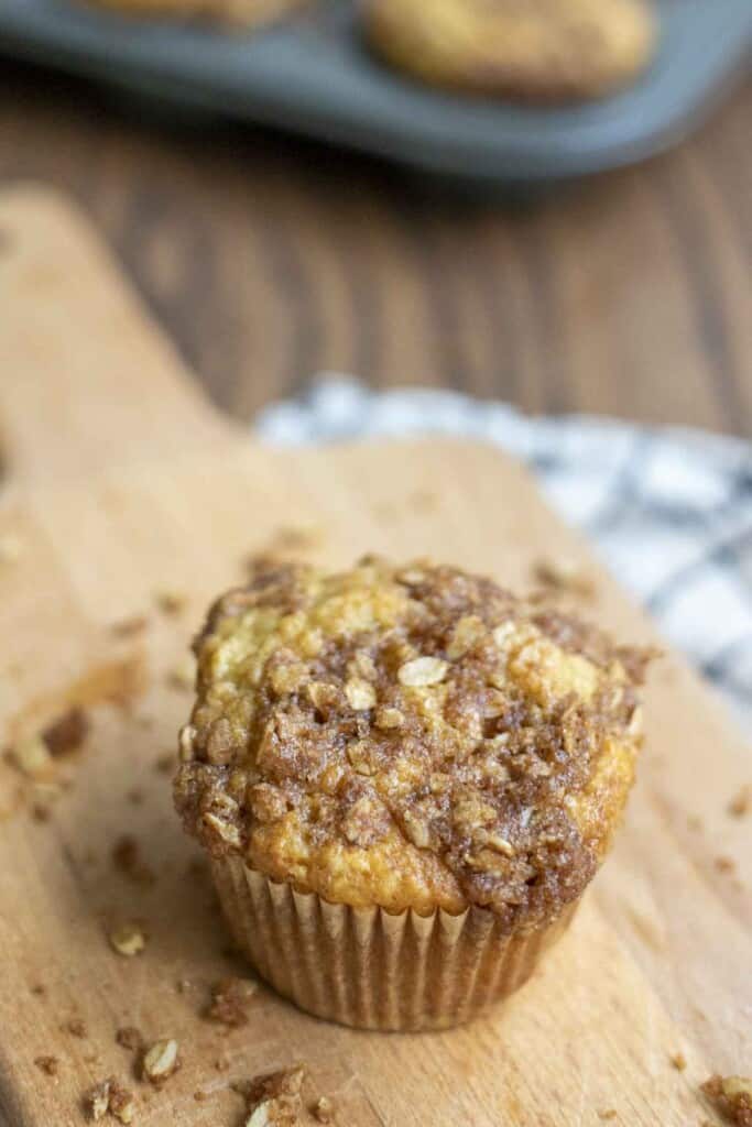 top view of oat crumble on a sourdough banana muffin on a small wood cutting board with crumble sprinkled about