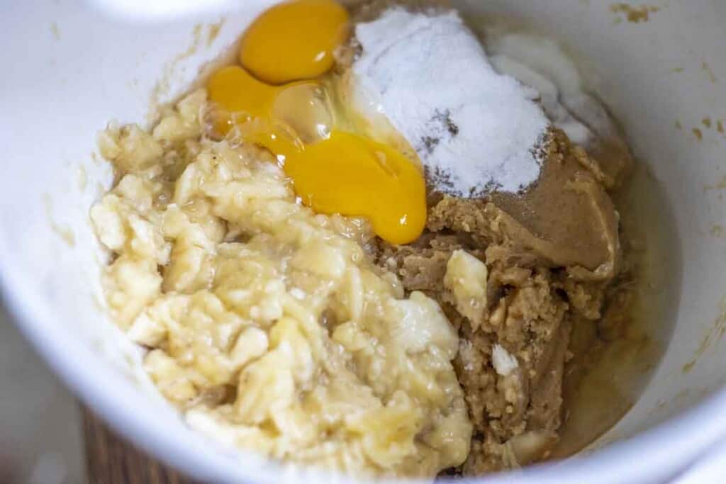 mashed banana, eggs, baking soda, baking powder, and salt with quick bread batter in a white bowl