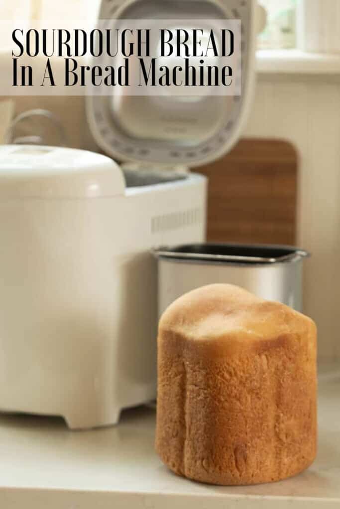 sourdough bread right out of the bread machine on a white countertop with the bread machine and baking pan in the background