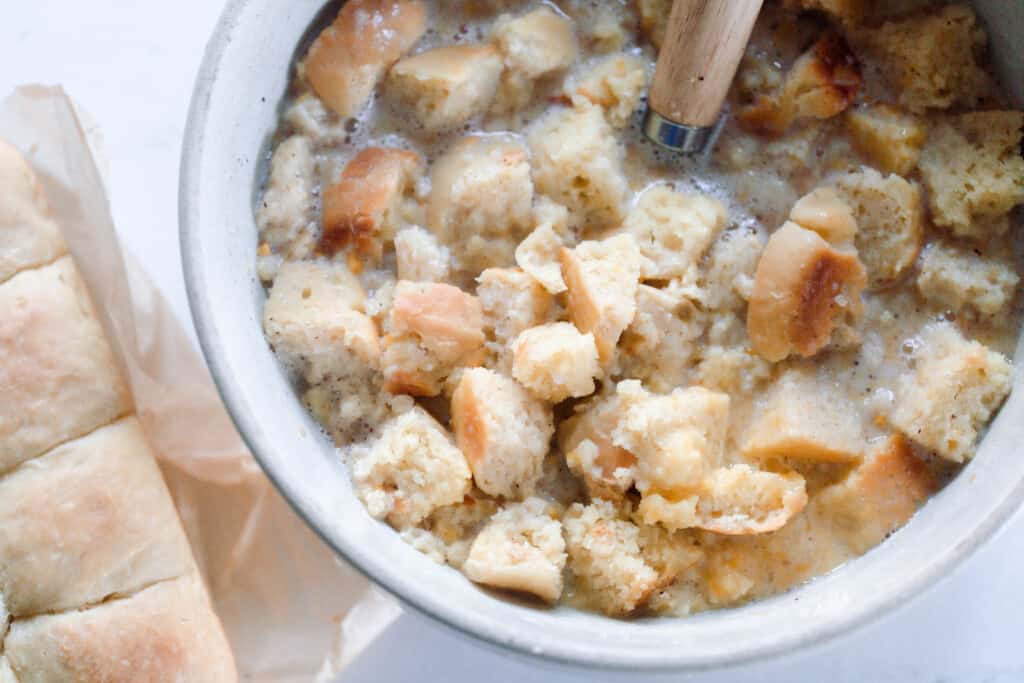 custard filling and cubed bread in a large white bowl with a dough whisk sitting in the bowl