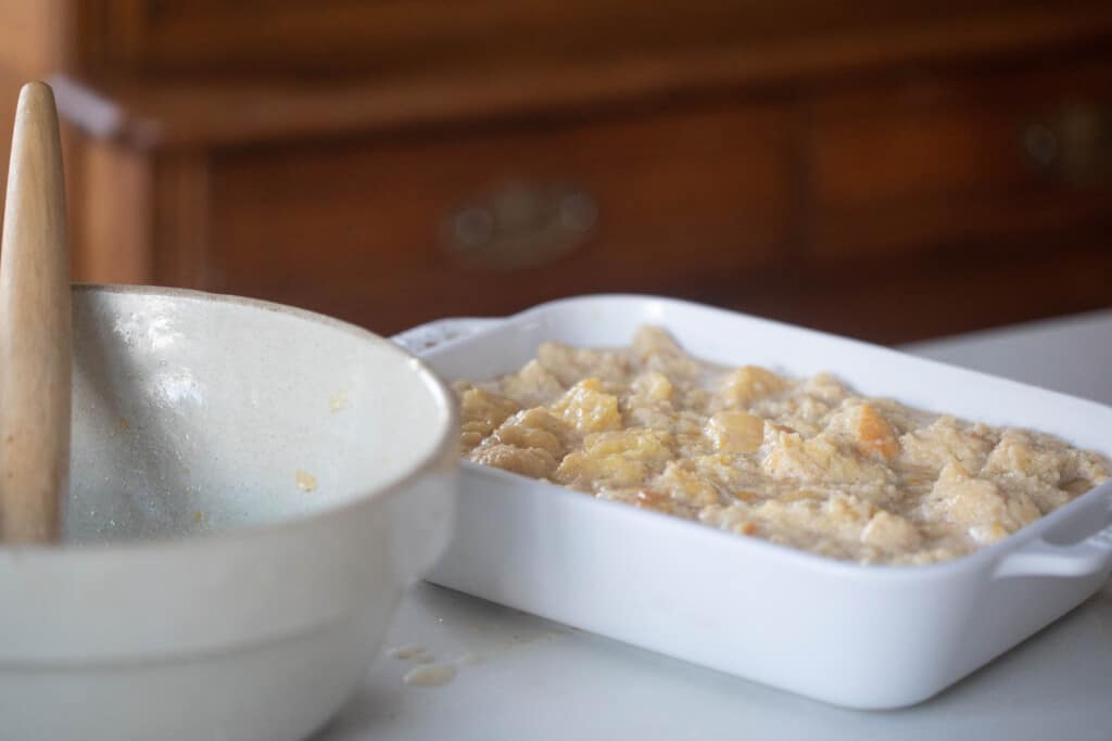 unbaked sourdough bread pudding in a white baking dish with a large bowl to the left.