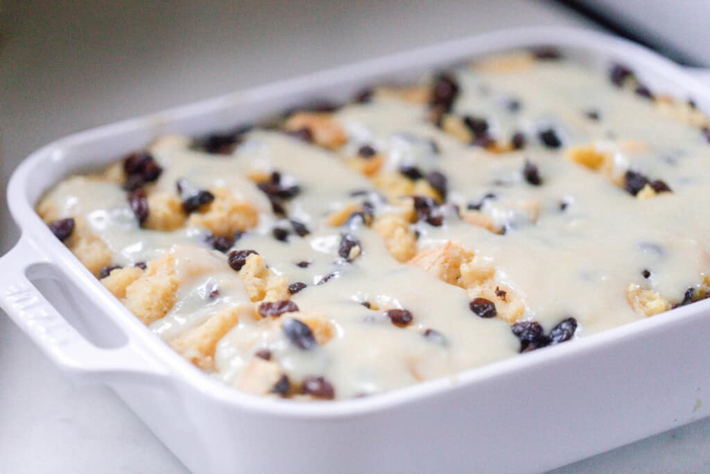 sourdough bread and butter pudding in a white baking dish covered with a raisins and a creamy sauce
