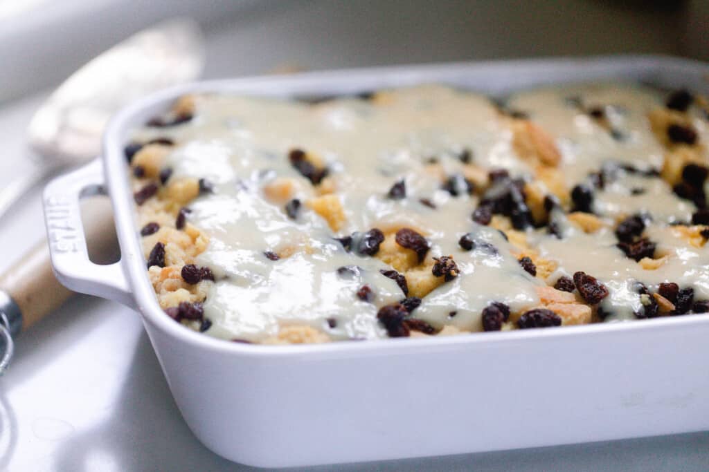 side view of sourdough bread pudding topped with raisins and a brea pudding sauce baked in a white baking dish