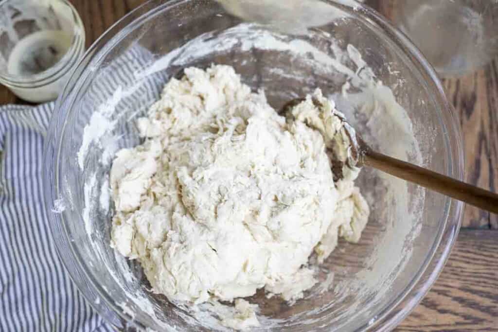 bread dough in a glass bowl with a wooden spoon