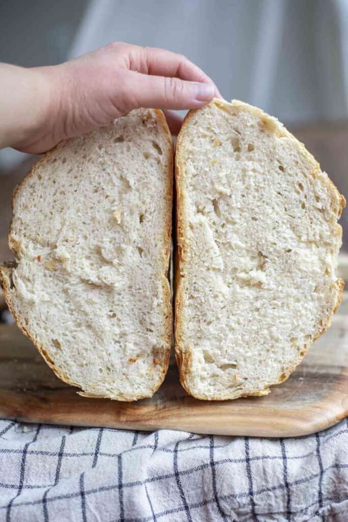 hand holding two halves of a loaf of sourdough discard bread on a wood cutting board on a black and white checked towel