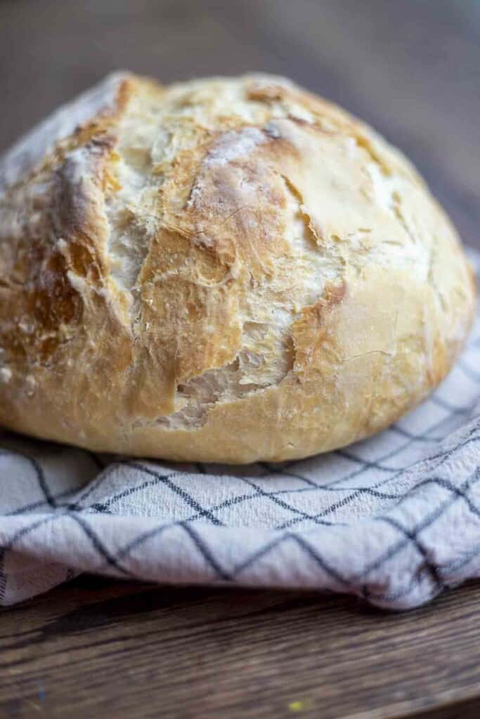 loaf of crusty sourdough discard bread on a white and black checked towel on a wood table