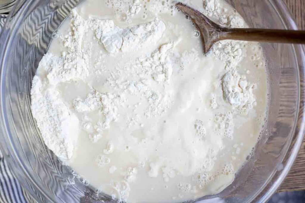 flour, water, yeast, salt, and sourdough starter in a glass bowl with a wooden spoon