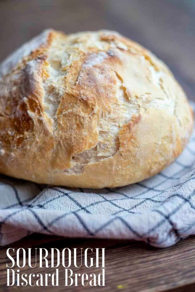 loaf of crusty sourdough discard bread on a white and black checked towel on a wood table