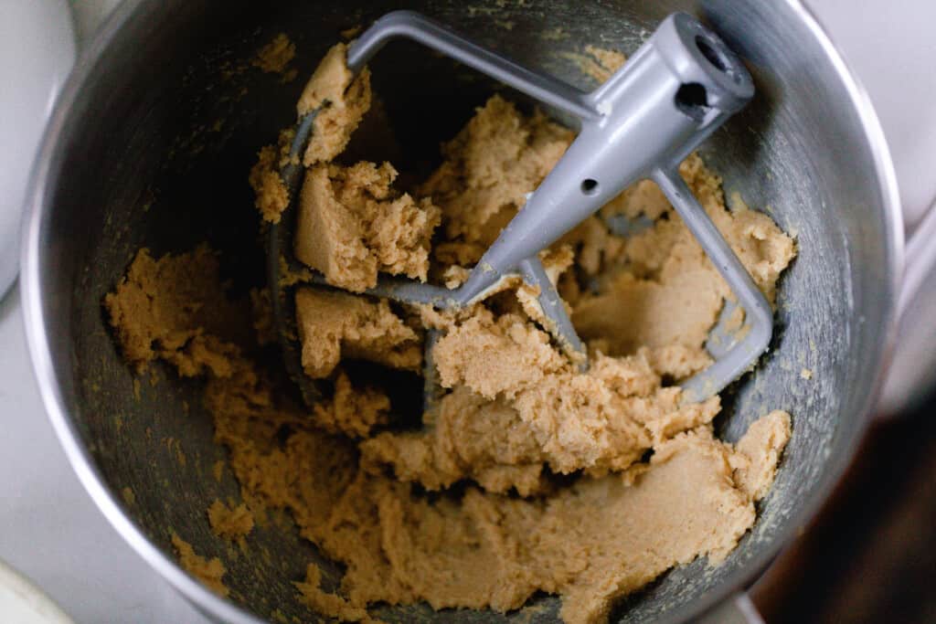 a stand mixer bowl with cookie dough and the mixer beater resting in the bowl