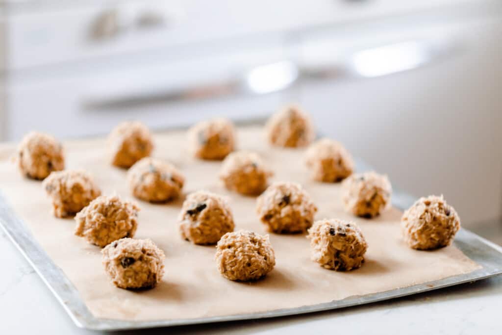 sourdough oatmeal cookie dough in balls on a parchment lined baking sheet in a white kitchen
