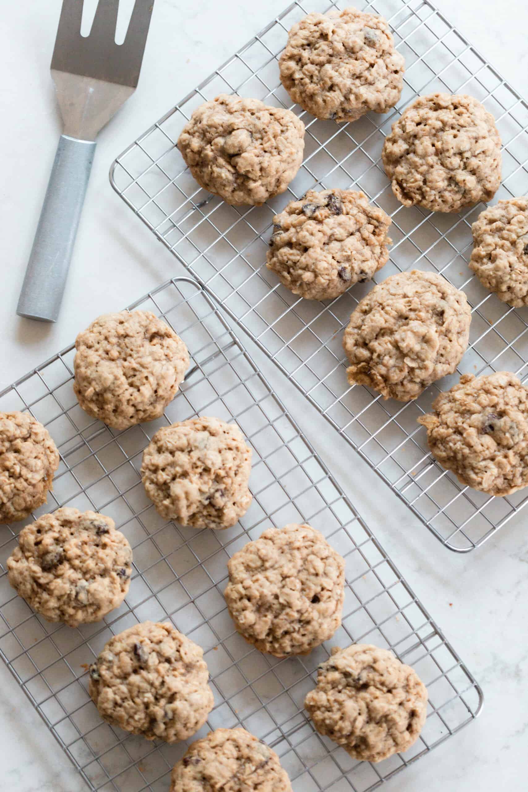 overhead photo of two wire racks full of oatmeal cookies on a white countertop with a metal spatula in the back corner