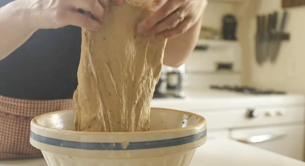 hand pulling up on dough from a bowl in a white kitchen