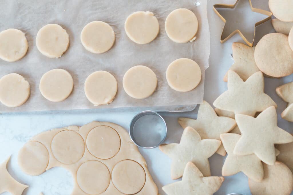 round sugar cookies cut and layer on a parchment lined baking sheet. The dough with more cookies cut out in the dough. 