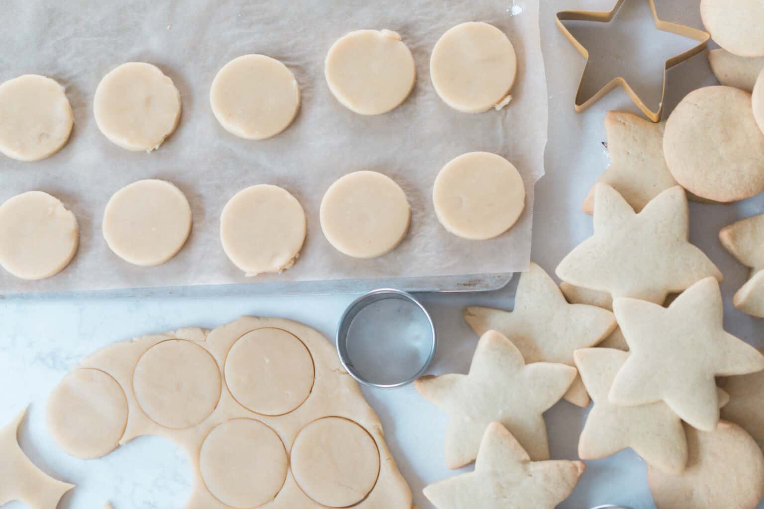 round sugar cookies cut and layer on a parchment lined baking sheet. The dough with more cookies cut out in the dough.