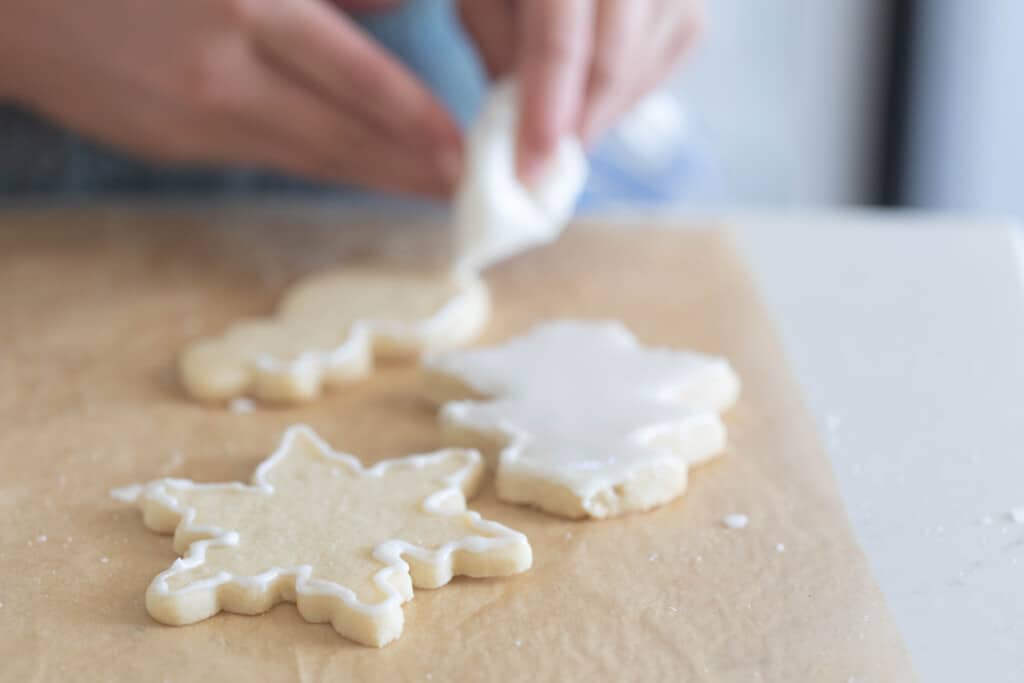 hands with an icing bag decorating sourdough sugar cookies on parchment paper