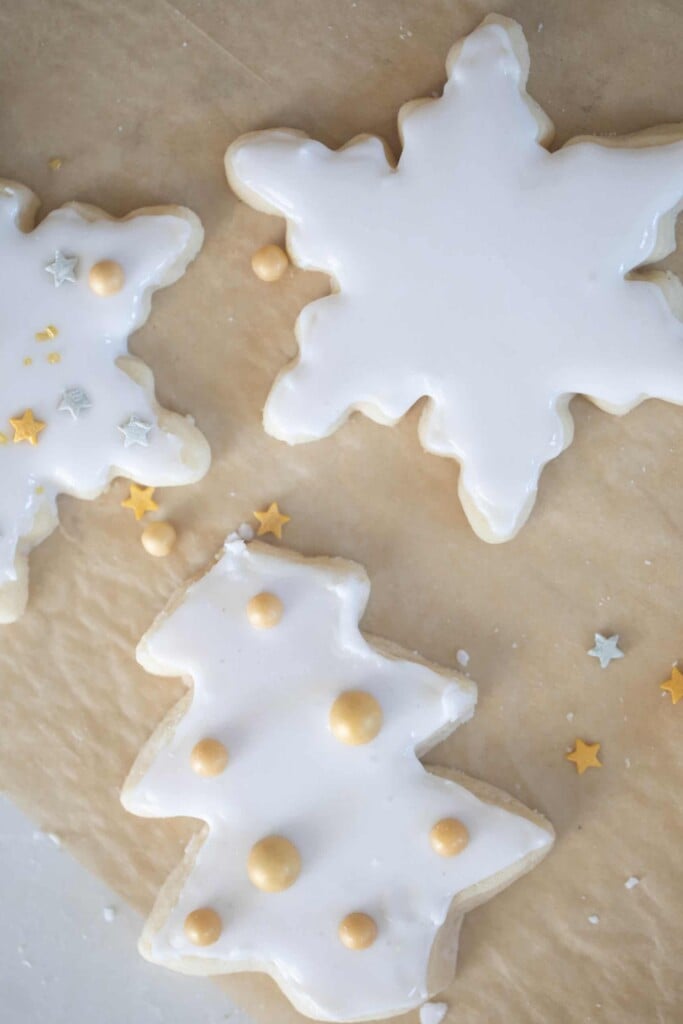 overhead photo of sourdough sugar cookies cut out in snowflakes and trees with white icing and gold balls on parchment paper