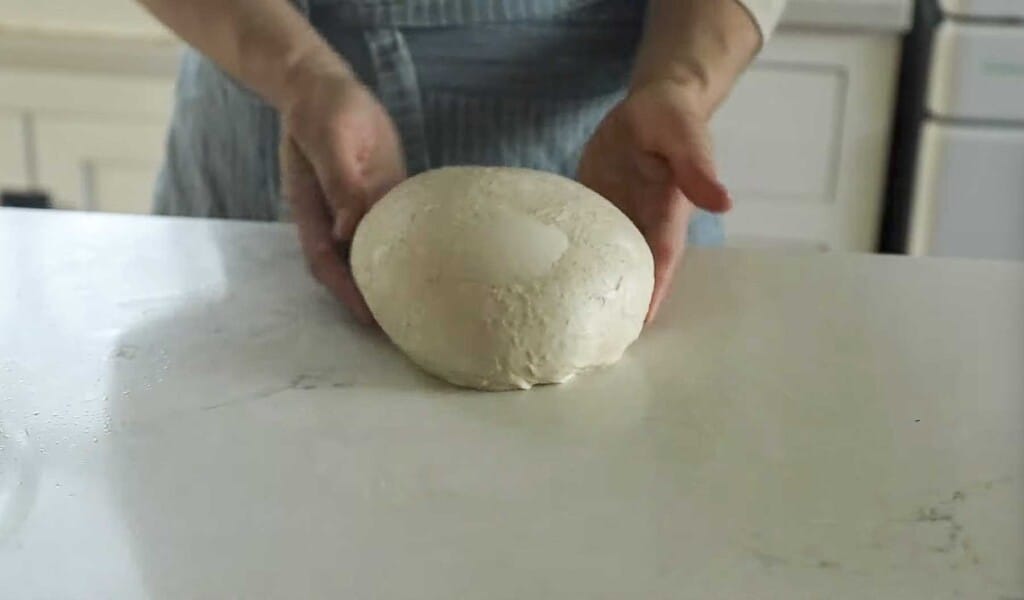 hands forming a boule on a white countertop