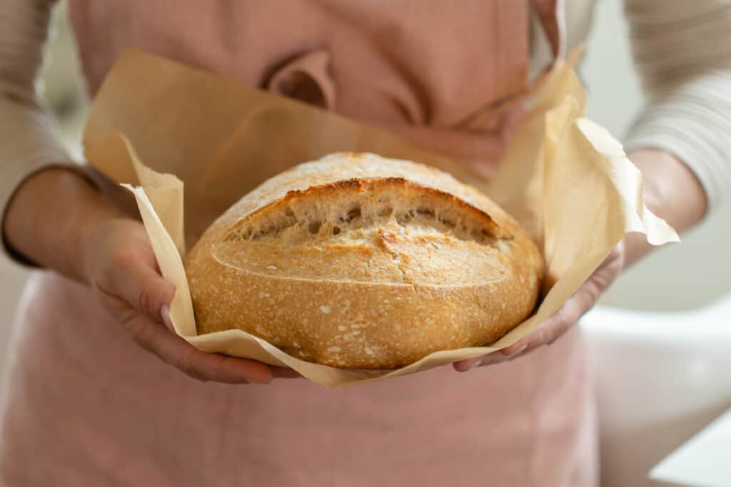 woman wearing a pink apron holding a loaf of spelt sourdough bread on parchment paper