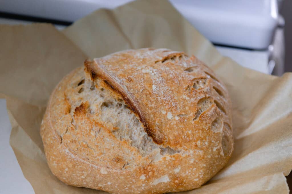 a loaf of sourdough bread made with spelt rests on parchment paper on top of a white stove