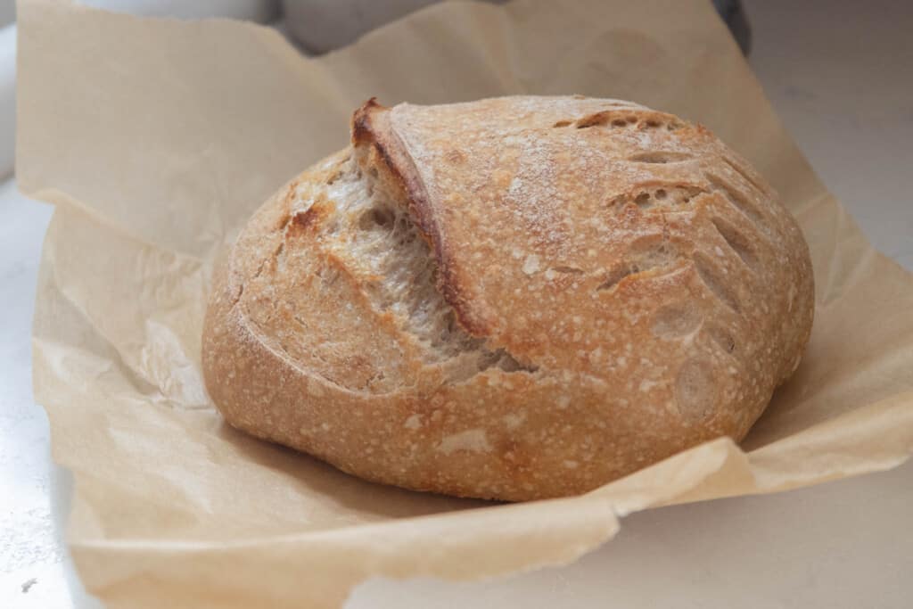 a boule of sourdough bread made with spelt on parchment paper on a white antique stove