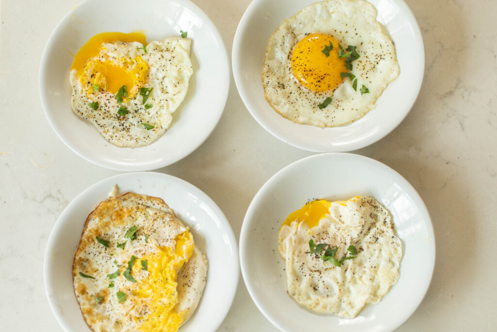 over easy, over-hard, over medium, and sunny side up eggs on white plates on a white countertop