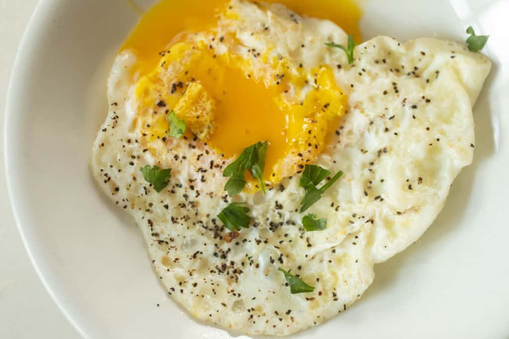 close up picture of an over-easy eggs with runny yolks topped with fresh herbs on a white plate