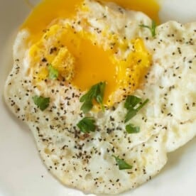 close up picture of an over-easy eggs with runny yolks topped with fresh herbs on a white plate