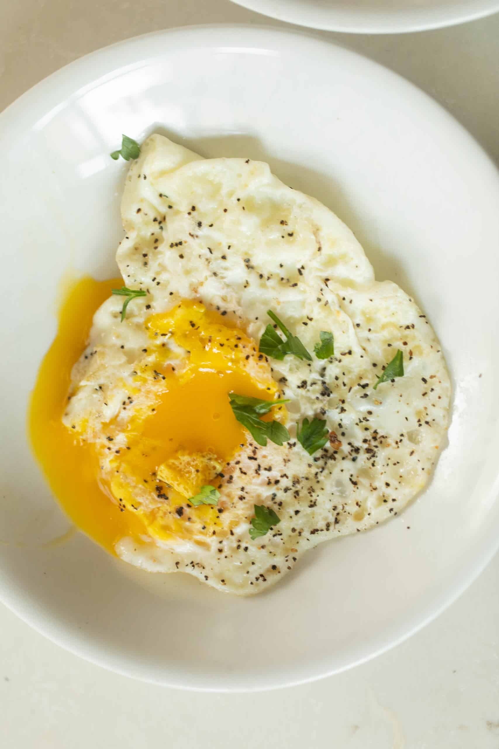 overhead photo of over easy eggs topped with fresh herbs on a white plate