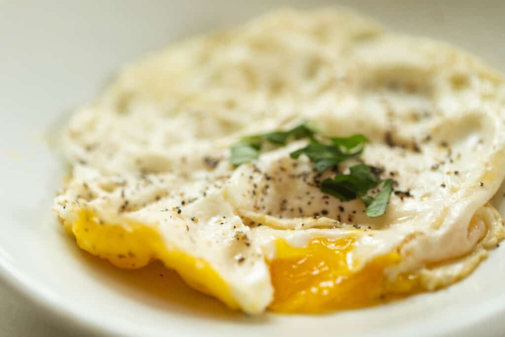 close up of a fried over medium egg topped with fresh basil on a white plate