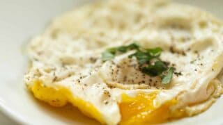 close up of a fried over medium egg topped with fresh basil on a white plate